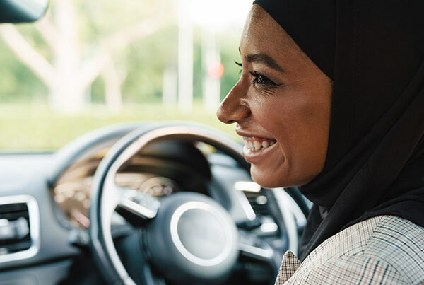 Smiling lady in hijab sits in driving seat of car, happy that she has used Zixty for her learner driver insurance.